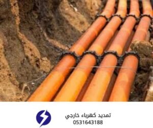 فني يقوم بتمديد مواسير كهرباء خارجية برتقالية اللون داخل خندق أرضي لتوصيل الكابلات.